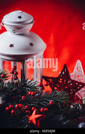 Lanterne blanc noël est debout avec une bougie allumée à l'aide d'une branche de sapin, et tricoter étoile en face de lui sur un fond rouge. fa noël Banque D'Images