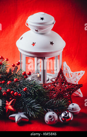 Lanterne blanc noël est debout avec une bougie allumée à l'aide d'une branche de sapin, et tricoter étoile en face de lui sur un fond rouge. fa noël Banque D'Images