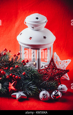 Lanterne blanc noël est debout avec une bougie allumée à l'aide d'une branche de sapin, et tricoter étoile en face de lui sur un fond rouge. fa noël Banque D'Images