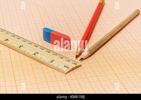 Sur un papier millimétrique il y a une règle en bois, une gomme et deux simples crayons Banque D'Images