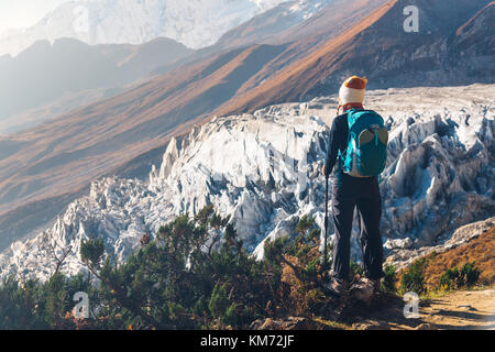 Jeune femme debout avec sac à dos sur le sommet de la montagne et à la recherche sur les belles montagnes et des glaciers au coucher du soleil. Paysage avec des roches, fille de neige Banque D'Images