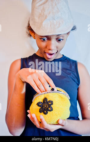 Jeune fille avec chapeau clair sourit joyeusement quand elle regarde dans son petit sac noir et jaune Banque D'Images