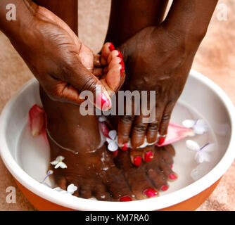 Femme africaine trempant ses pieds et mains dans un bol d'eau et de pédales de fleurs Banque D'Images