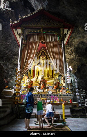 Kanchanaburi, THAÏLANDE - 12 juillet 2017 : trois visiteurs devant une statue de Bouddha au wat ban tham cave temple, qui est le formulaire d'entrée comme un dragon's mouth. Banque D'Images