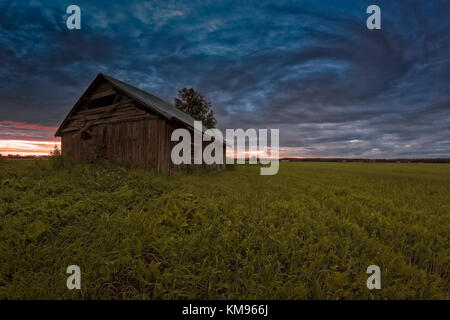 Une vieille grange chambre s'sous un ciel très dramatique, à la limite nord de la Finlande. Le coucher du soleil d'été le ciel de couleurs encore plus spectaculaire. Banque D'Images