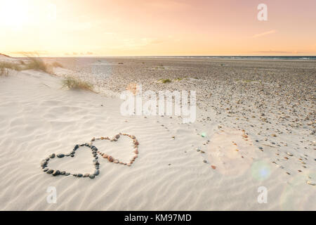 Cailloux disposés en forme de deux cœurs sur plage sable ondulations avec beau coucher du soleil. Banque D'Images