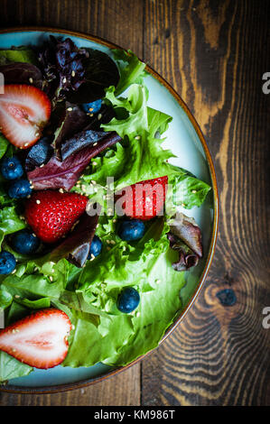 Salade verte aux fruits rouges sur fond de bois Banque D'Images