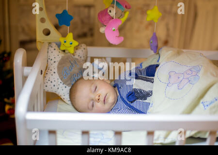 Adorable bébé nouveau-né garçon, dormant dans un lit bébé dans la nuit. Petit garçon au pyjama rayé bleu faire la sieste dans une pièce sombre, la décoration de Noël dans la chambre, Banque D'Images