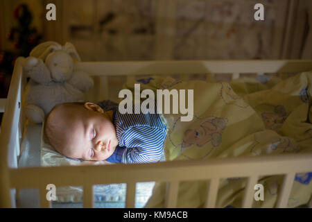 Adorable bébé nouveau-né garçon, dormant dans un lit bébé dans la nuit. Petit garçon au pyjama rayé bleu faire la sieste dans une pièce sombre, la décoration de Noël dans la chambre, Banque D'Images