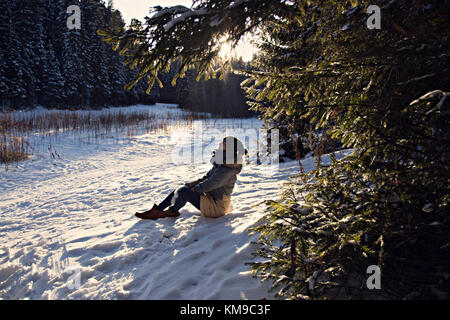 La figure d'une jeune fille dans une parka, un chapeau, des mitaines, assis dans l'hiver la forêt enneigée Banque D'Images