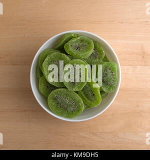 Vue de dessus quelques tranches de kiwi dans un bol blanc sur un comptoir en bois. Banque D'Images