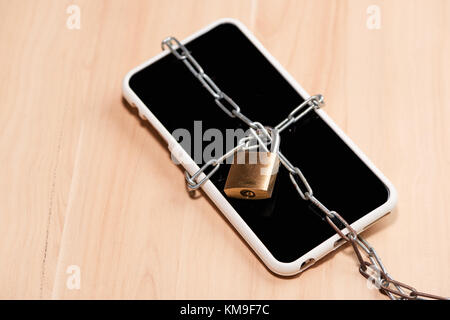 Chaîne liée smartphone avec verrouillage sur table en bois. Banque D'Images