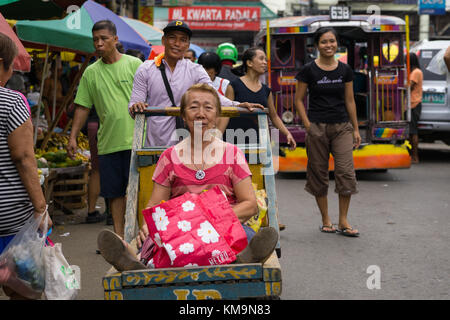 Une image humoristique d'une femme assise sur un chariot poussé par un homme à travers le marché du carbone, Cebu City Banque D'Images