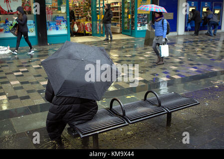 Fille avec parapluie noir assis sur le banc de la rue jour pluvieux humide Sauchiehall Street, Glasgow, Glasgow City, Royaume-Uni Banque D'Images