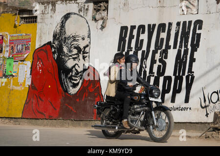 Couple sur moto ride passé sur la construction murale montrant le moine bouddhiste à côté de message de recyclage Banque D'Images