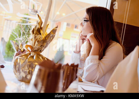 Jeune brunette assis dans un restaurant et en regardant par la fenêtre Banque D'Images