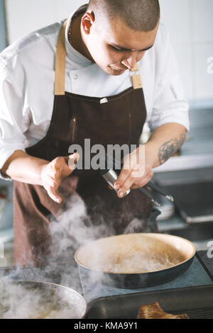 Young attractive male cook avec une préparation uniforme sause de viande. Banque D'Images