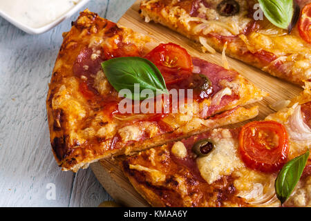 Tranches de pizza au bacon, les olives et les tomates sur une planche à découper. Banque D'Images