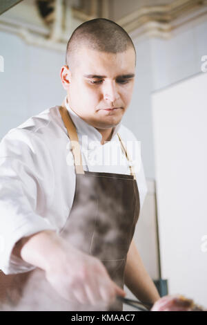 Young attractive male cook avec la préparation d'un uniforme de la viande. Banque D'Images