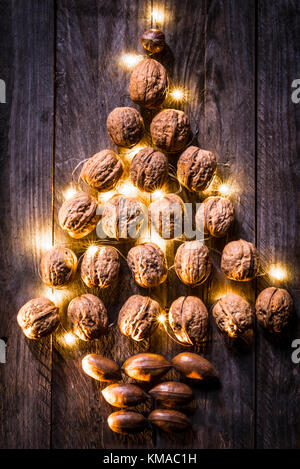 Noix et noix de pécan disposés sur un fond de bois en une forme d'arbre de Noël avec des lumières dorées dispersées parmi eux. Banque D'Images