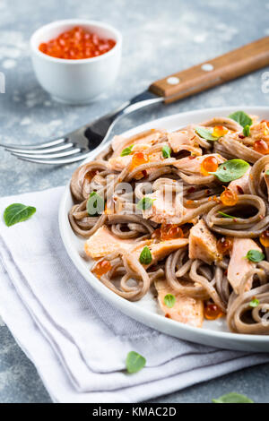 Soba japonais traditionnel cuisiné avec le saumon et garnie de feuilles de basilic et de caviar Banque D'Images