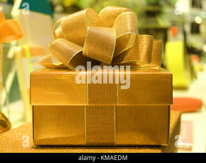 Vue frontale d'un or brillant carré boîte-cadeau avec pink ribbon bow, l'arrière-plan flou Banque D'Images