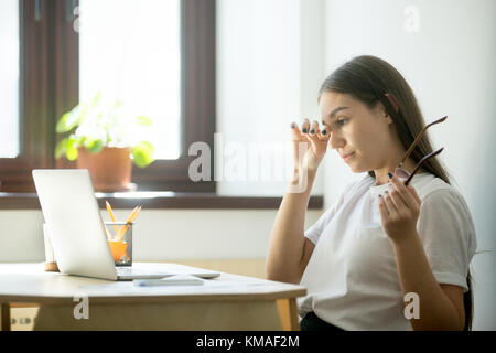 Jeune femme avec des yeux fatigués holding glasses. femme gêne de long portant des lunettes derrière un coffre sur le lieu de travail visuelle. Banque D'Images