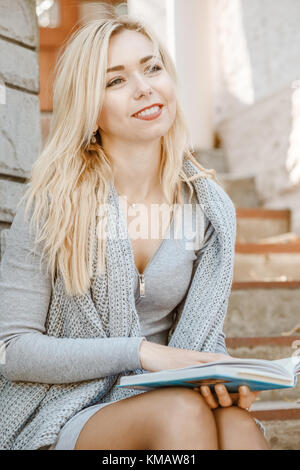 Jeune femme élégante assise dans les escaliers à l'extérieur aime une lecture de livre Banque D'Images
