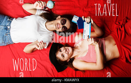 Deux cheerful friends girls holding les passeports, les billets d'avion et globe couché sur un lit rouge, intérieur travel concept Banque D'Images