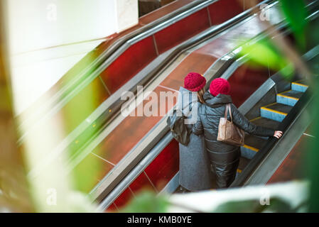 Vue arrière deux filles monter sur l'escalator dans le métro. escaliers mécaniques dans le métro. déménagement jusqu'escalier. Bouilloire escalator. vue à travers la verdure. soft focus sélectif. Banque D'Images