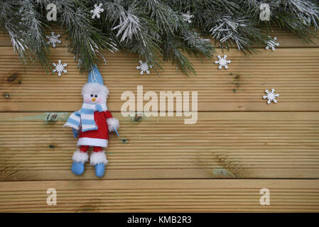 Arbre de Noël de la saison d'hiver avec la neige et garland avec fond en bois naturel rustique et de décoration pendaison heureux bonhomme en rouge et bleu Banque D'Images