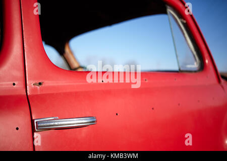 Poignée de porte et fenêtre latérale d'une vieille voiture rouge vintage avec garniture de perles et manquant sur la porte et la corrosion Banque D'Images