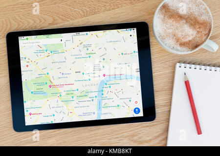 L'application Google Maps fonctionnalités sur un iPad tablet device qui repose sur une table en bois à côté d'un bloc-notes et un crayon et une tasse de café (rédaction uniquement). Banque D'Images