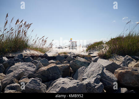 Plage surveillée de la cabine côté derrière l'herbe et de grands rochers gris, tourné à partir de l'angle faible contre le ciel bleu Banque D'Images