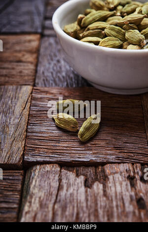 Cardamomes vertes dans un bol sur fond de bois rustique. Banque D'Images