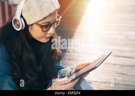 Voir ci-dessus de belle jeune étudiant Asie recherche d'informations en ligne avec une tablette numérique assis sur le plancher de bois du pont. Banque D'Images