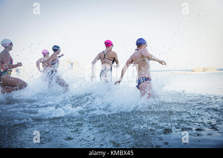 Les nageurs en eau libre féminin en marche et de s'éclabousser dans océan surf Banque D'Images