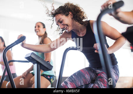 Jeune femme souriante et ludique utilisant un vélo elliptique dans la salle de gym Banque D'Images