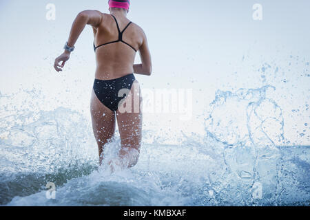 Les nageurs en eau libre féminin en marche et de s'éclabousser dans océan surf Banque D'Images