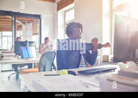 Male design professional bras étirement at computer in office Banque D'Images