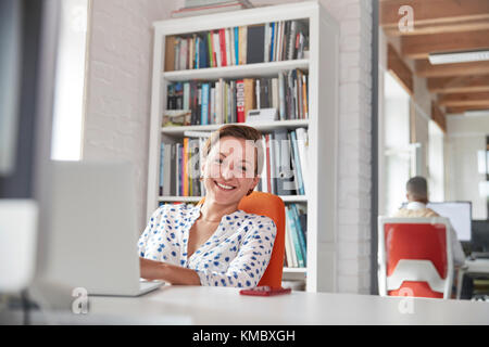 Portrait souriant, femme d'affaires confiante travaillant à un ordinateur portable au bureau Banque D'Images