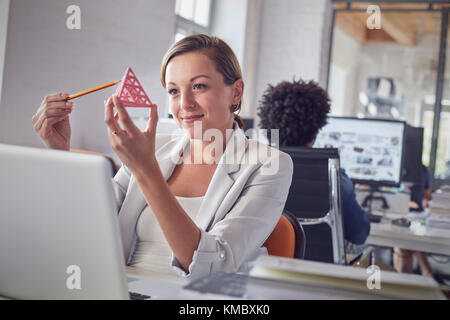 Femme souriante design professionnel examinant le prototype de triangle à l'ordinateur portable dans bureau Banque D'Images