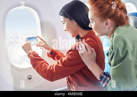 Jeunes femmes amis utilisant un téléphone avec appareil photo à la fenêtre de l'avion Banque D'Images