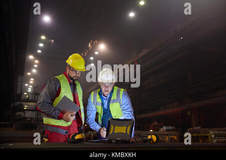 Steelworkers utilisant un ordinateur portable dans une usine en acier foncé Banque D'Images