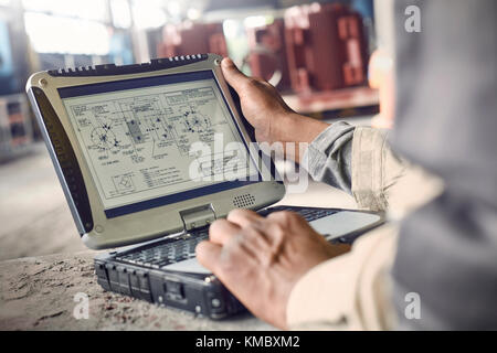 Ingénieur utilisant un ordinateur portable, en examinant les plans dans l'aciérie Banque D'Images