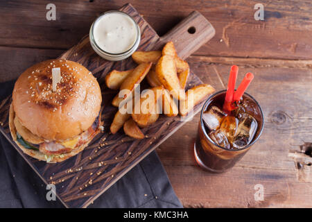 Un hamburger savoureux avec des en-cas sous forme de pommes de terre avec une sauce à l'ail blanc et un verre de Coca-Cola froid. Hamburger juteux avec des rondelles d'oignon, du bacon et du fromage o Banque D'Images