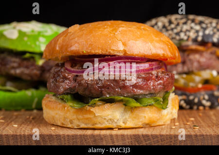 Gros plan d'un ensemble de trois mini-hamburgers faits maison avec du bœuf en marbre et des légumes sur une planche en bois. Banque D'Images
