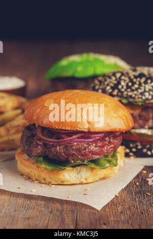 Gros plan d'un ensemble de trois mini-hamburgers faits maison avec du bœuf en marbre et des légumes sur une planche en bois. Banque D'Images