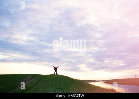 Homme heureux avec mains soulevées par le fleuve sur un fond de ciel coucher de soleil. Banque D'Images