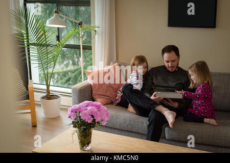 Père et filles utilisant une tablette numérique dans le salon Banque D'Images